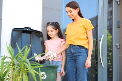 Mother and her daughter throwing paper into recycling bin outdoors