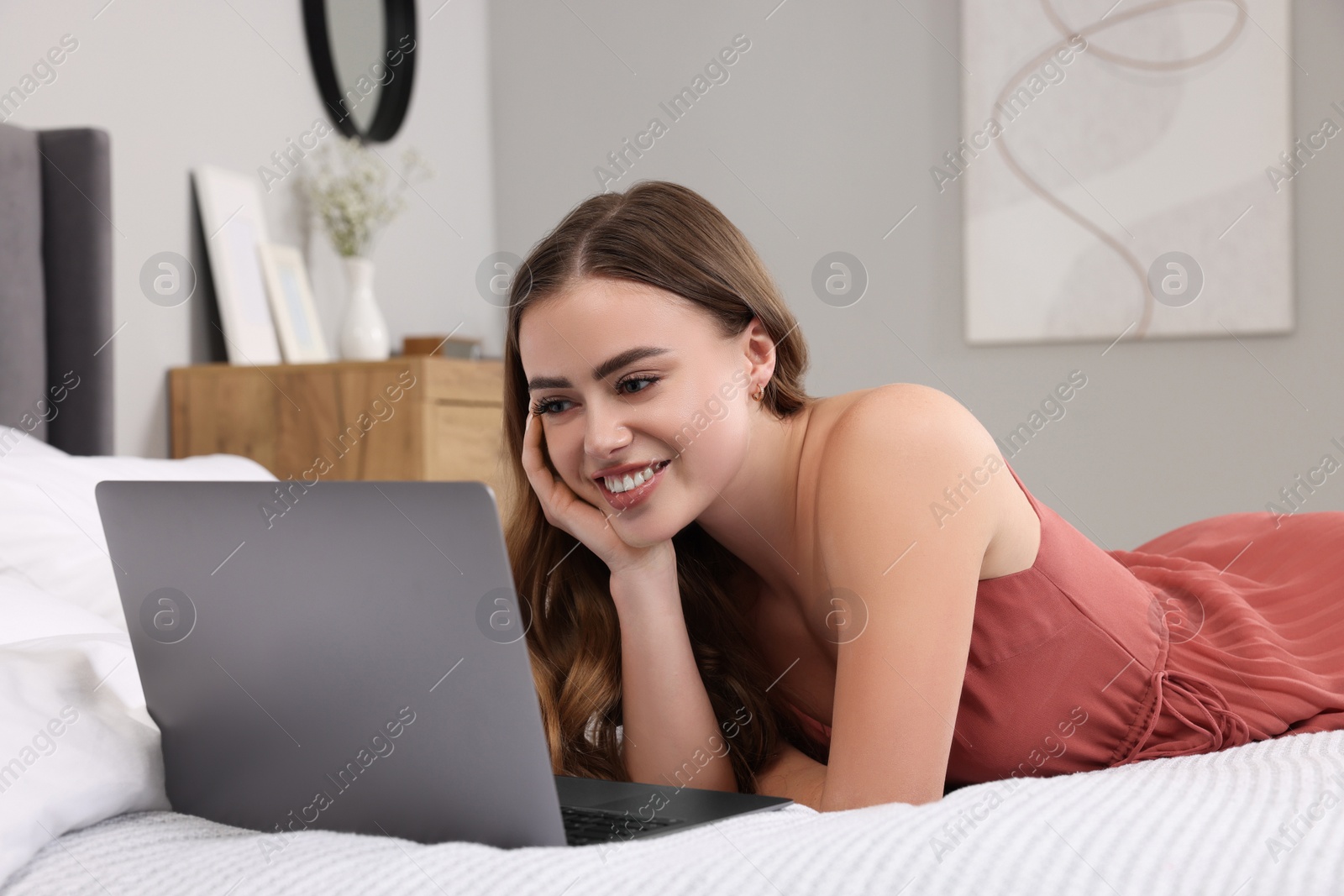 Photo of Happy woman with laptop on bed in bedroom