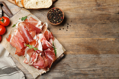 Photo of Pile of tasty prosciutto on wooden table, flat lay. Space for text