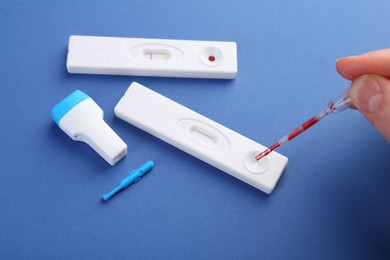 Photo of Woman dropping blood sample onto disposable express test cassette with pipette on blue background, closeup