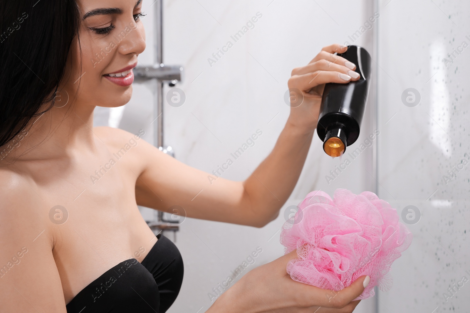 Photo of Young woman pouring gel onto mesh pouf in shower at home