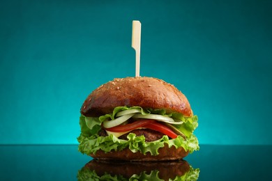 Photo of Delicious vegetarian burger on mirror surface against teal background