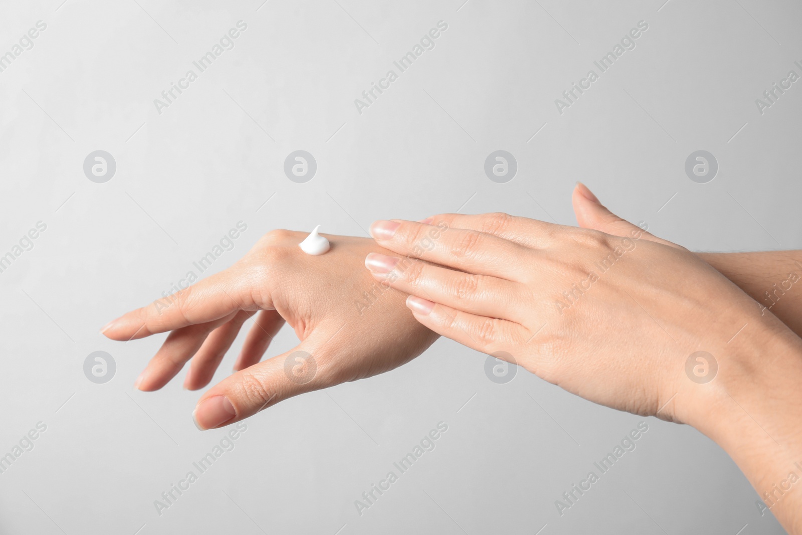 Photo of Woman applying hand cream on light background, closeup