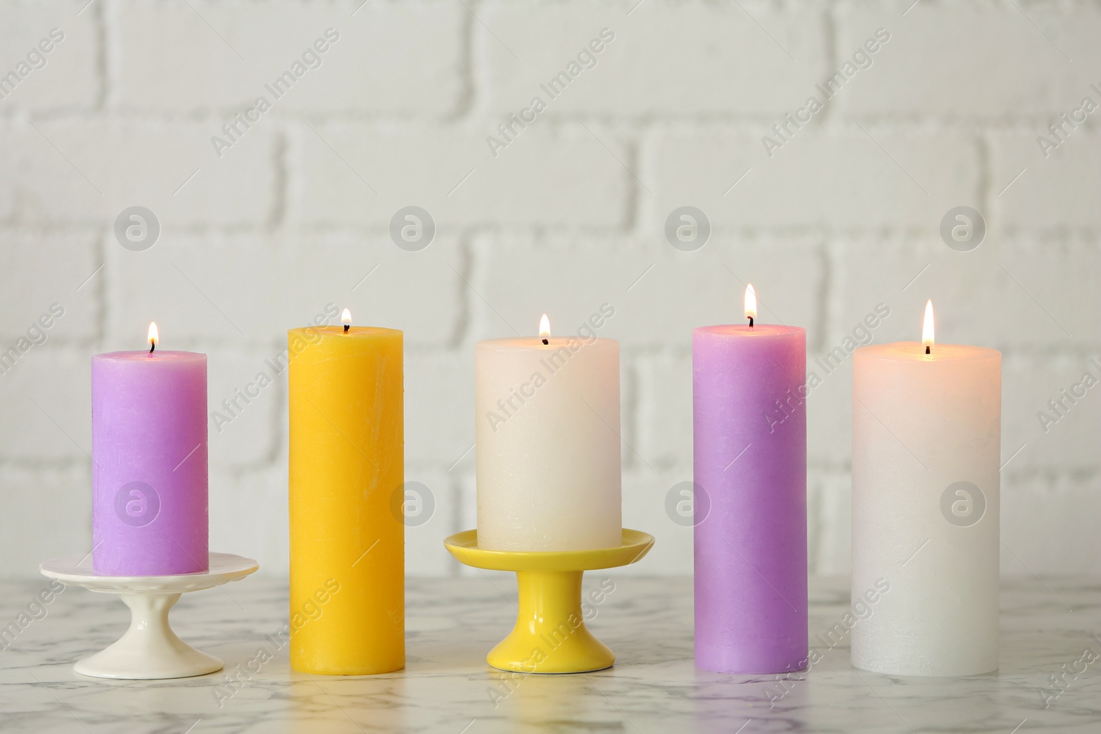 Photo of Different decorative wax candles on table against brick wall