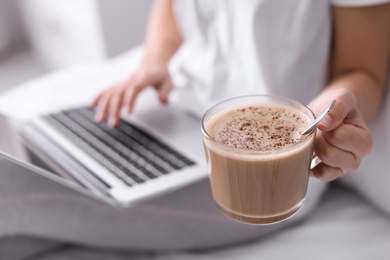 Photo of Woman with cup of morning coffee working on laptop indoors, closeup