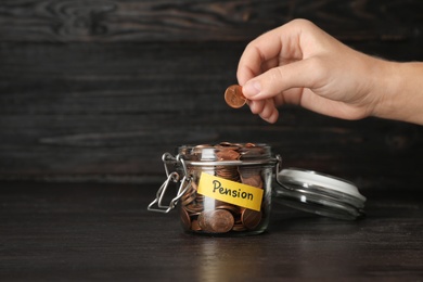Photo of Woman putting coin in glass jar with label "PENSION" on table, closeup. Space for text