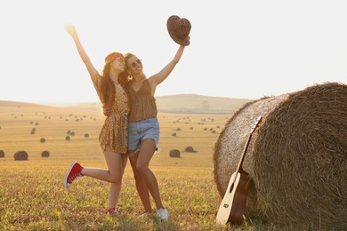 Happy hippie women near hay bale and guitar in field