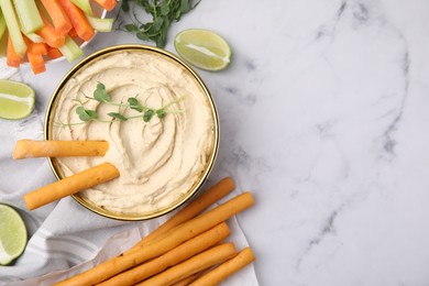 Photo of Delicious hummus with grissini sticks served on white marble table, flat lay. Space for text