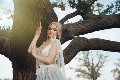 Photo of Beautiful girl wearing fairy dress near tall tree outdoors
