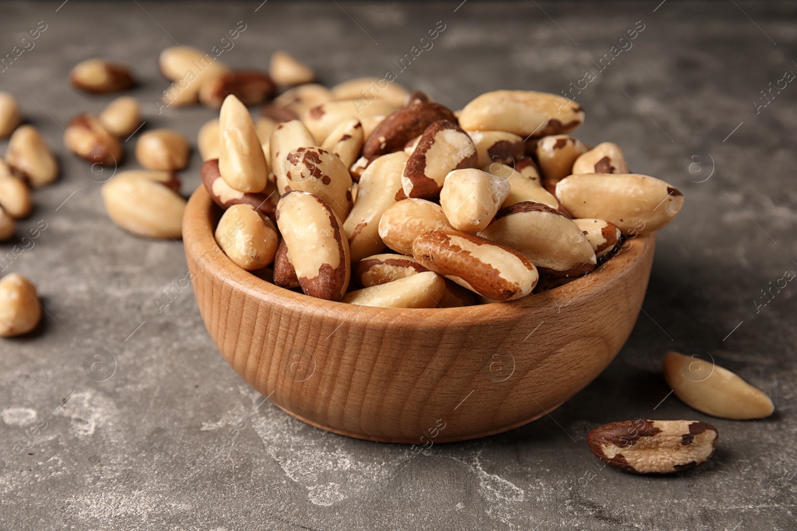 Photo of Bowl with tasty Brazil nuts on grey table