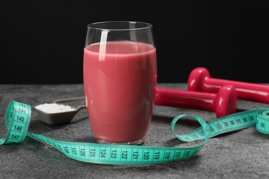 Photo of Tasty shake, measuring tape, dumbbells and powder on stone table against black background. Weight loss