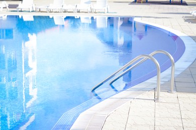 Photo of Outdoor swimming pool with ladder and handrails on sunny day