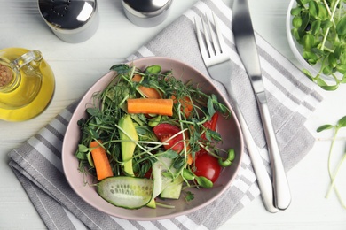 Salad with fresh organic microgreen in bowl on white table, flat lay