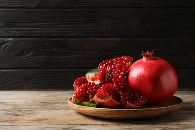 Photo of Plate with ripe pomegranates on wooden table against dark background, space for text