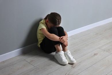 Photo of Child abuse. Upset girl sitting on floor near grey wall