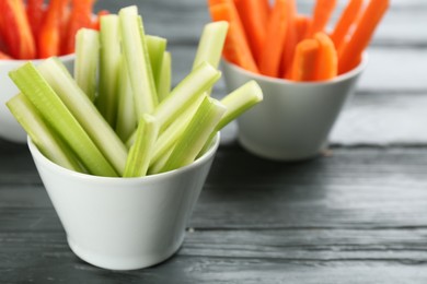 Photo of Celery and other vegetable sticks in bowls on grey wooden table, closeup