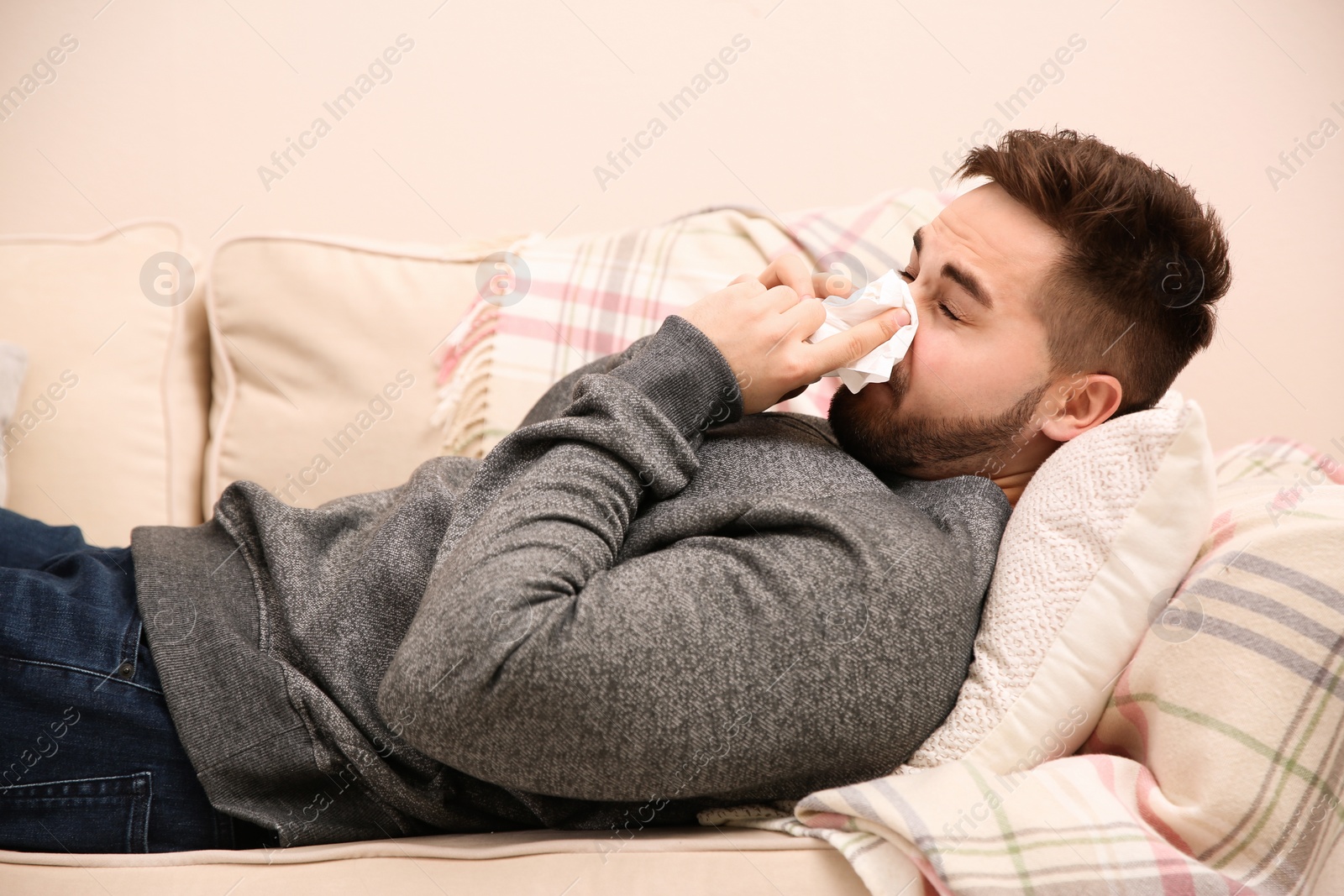 Photo of Sick young man sneezing at home. Influenza virus