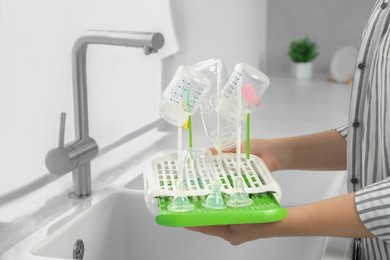 Photo of Woman holding dryer with baby bottles and nipples in kitchen, closeup