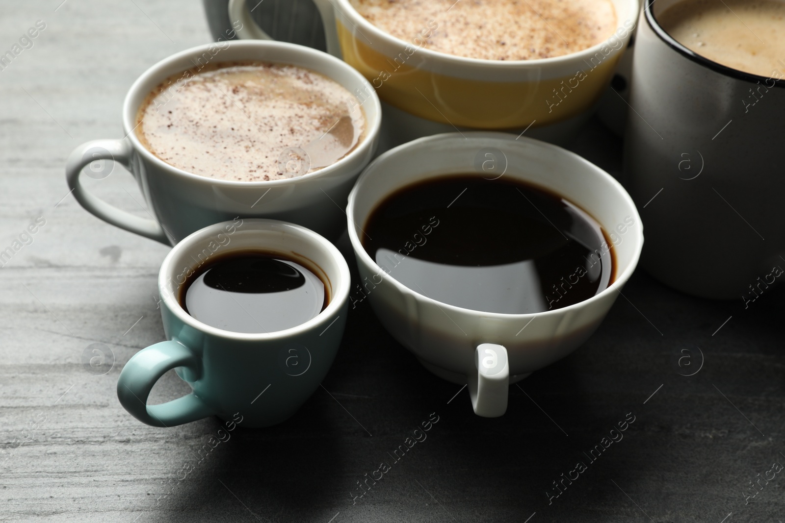 Photo of Many cups of different coffees on slate table, closeup