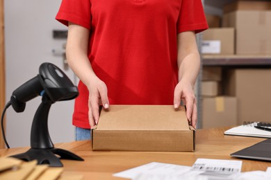 Photo of Post office worker packing parcel at wooden table indoors, closeup