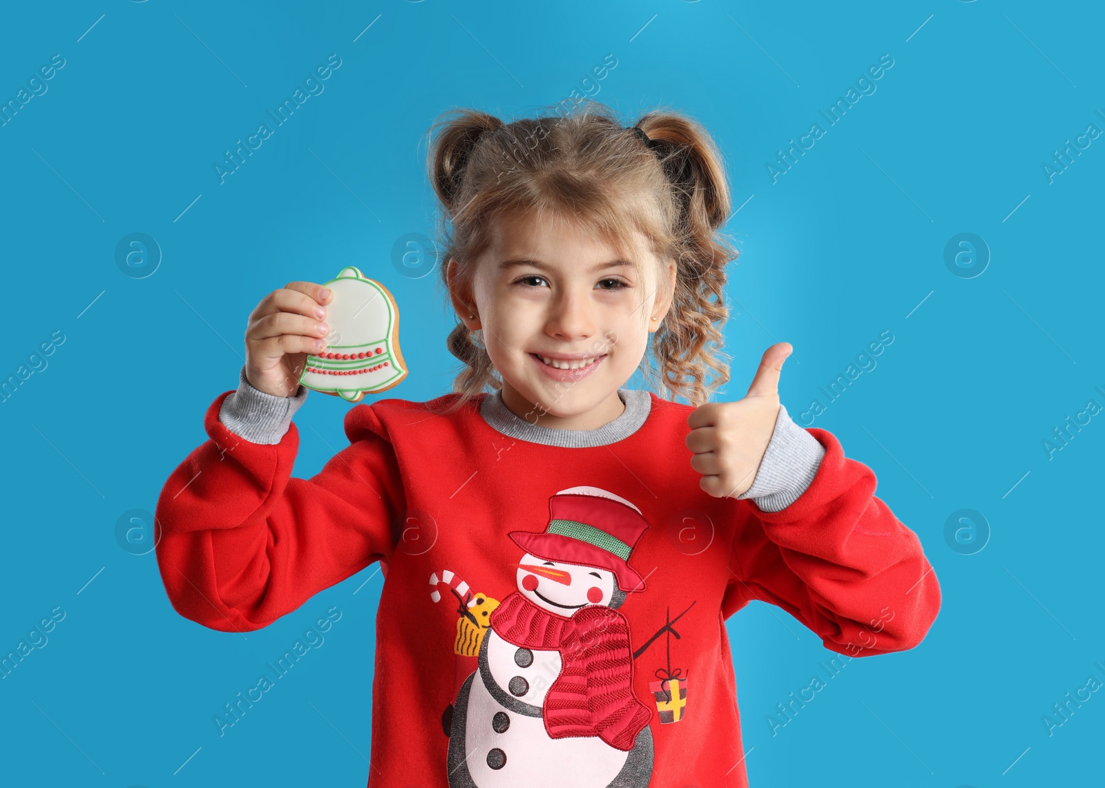 Photo of Cute little girl with Christmas gingerbread cookie on light blue background