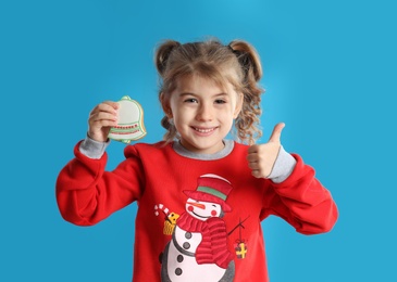 Cute little girl with Christmas gingerbread cookie on light blue background