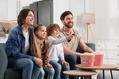 Photo of Happy family watching TV with popcorn on sofa at home