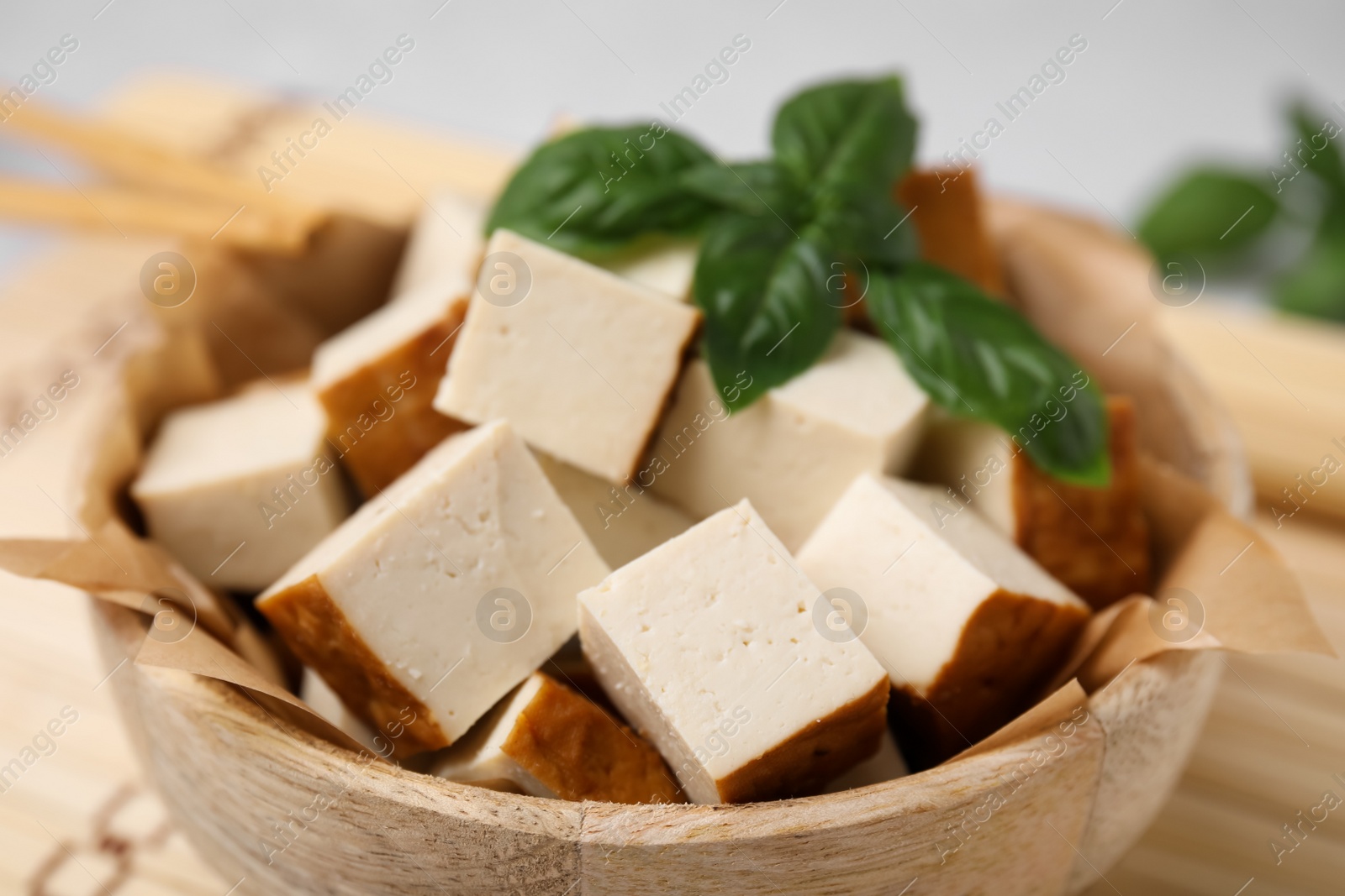 Photo of Bowl of smoked tofu cubes and basil on bamboo mat, closeup