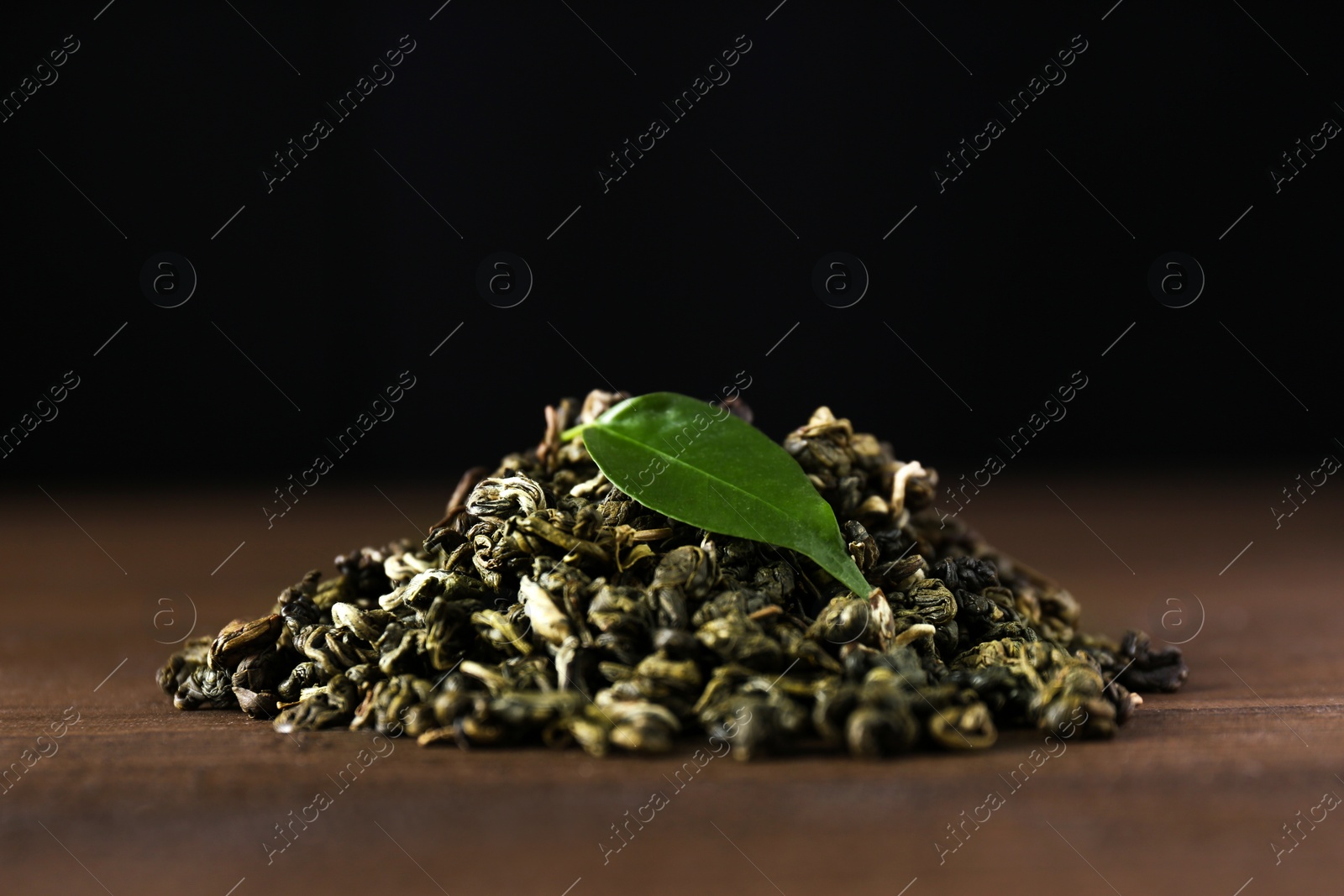 Photo of Heap of dried green tea leaves on wooden table, closeup