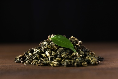 Photo of Heap of dried green tea leaves on wooden table, closeup