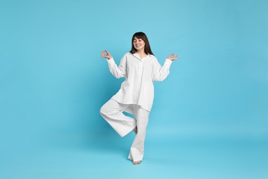 Photo of Happy woman in pyjama meditating on light blue background