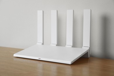 New modern Wi-Fi router on wooden table near white wall