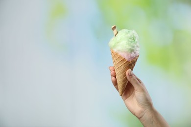 Photo of Woman holding waffle cone with cotton candy on blurred background, closeup. Space for text