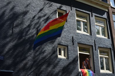 AMSTERDAM, NETHERLANDS - AUGUST 06, 2022: Building facade with bright LGBT pride flags and man looking out of window at parade