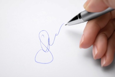 Woman writing her signature with pen on sheet of white paper, closeup