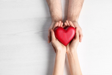 Photo of Couple holding decorative heart on white wooden background, top view