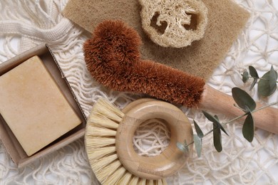 Cleaning brushes, sponge, loofah, soap bar and eucalyptus leaves on table, top view