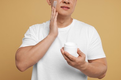 Photo of Man applying cream onto his face on light brown background, closeup