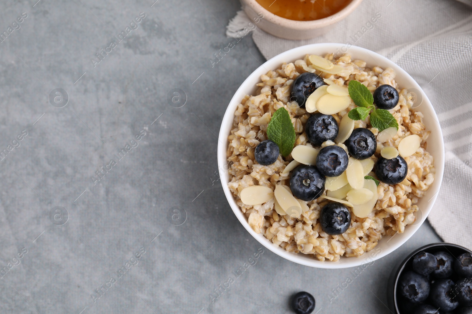 Photo of Tasty oatmeal with blueberries, mint and almond petals in bowl on grey table, flat lay. Space for text