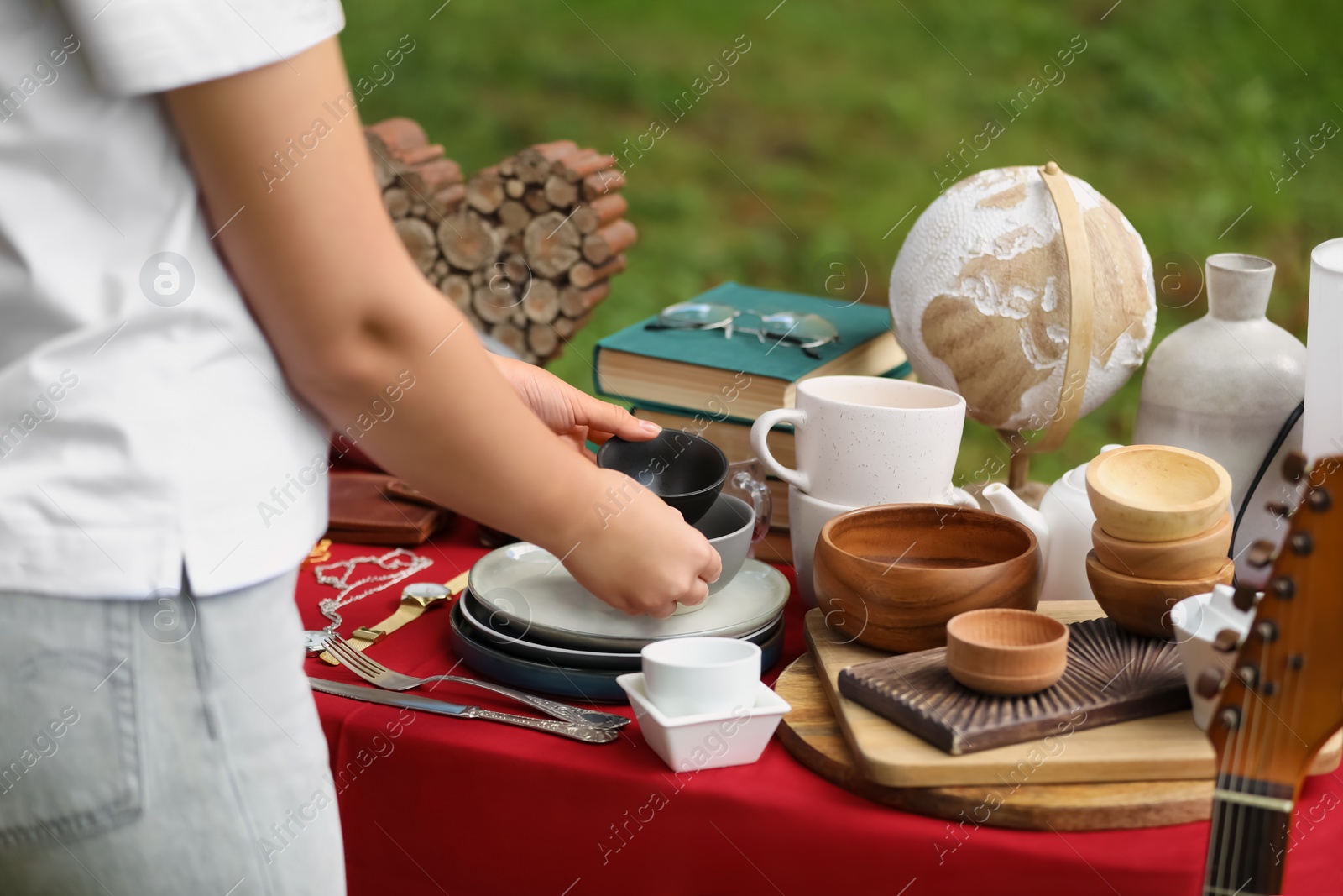 Photo of Woman holding beautiful bowls near table with different items on garage sale, closeup