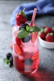 Photo of Delicious strawberry lemonade with soda water, mint and blackberries on grey table. Fresh summer cocktail