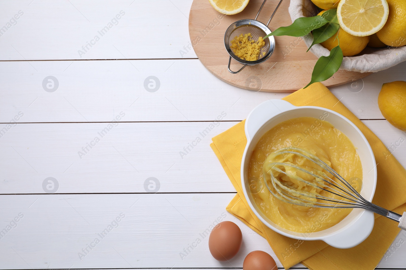 Photo of Delicious lemon curd in bowl, ingredients, whisk and sieve on white wooden table, flat lay. Space for text