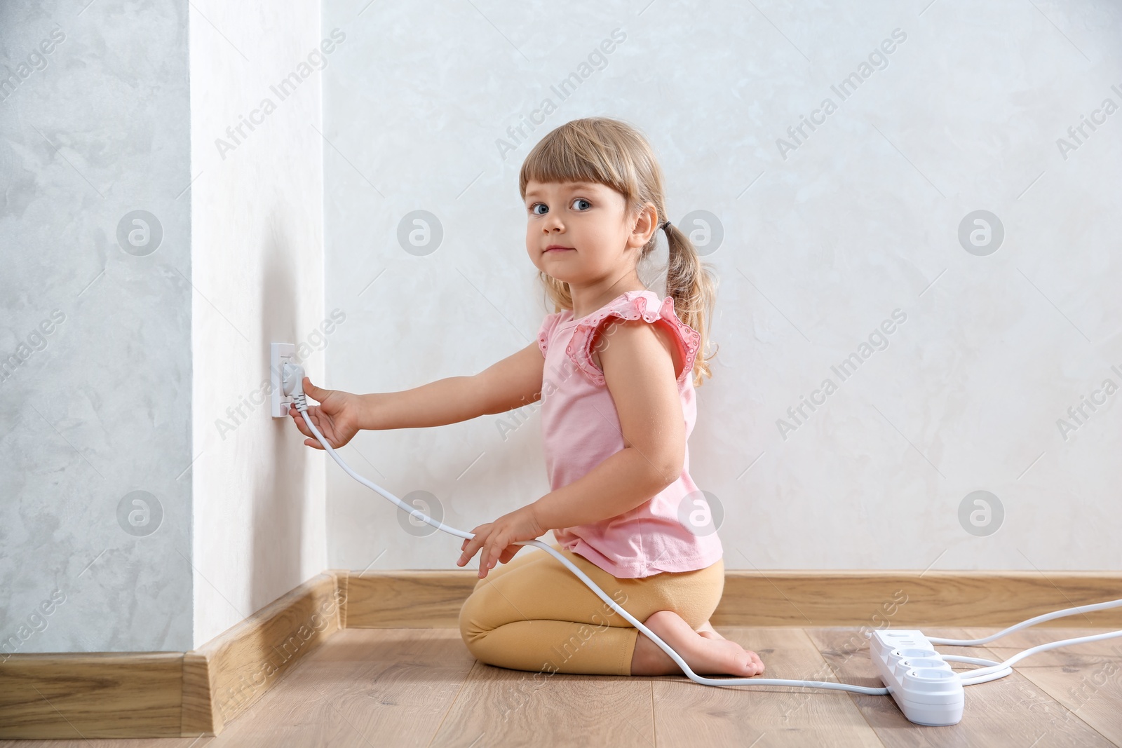 Photo of Little child playing with electrical socket and power strip plug at home. Dangerous situation