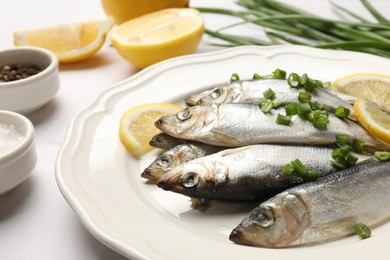 Photo of Fresh raw sprats, green onion, spices and cut lemon on white table, closeup