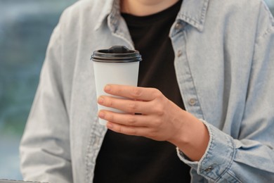Woman holding takeaway paper cup at table, closeup. Coffee to go