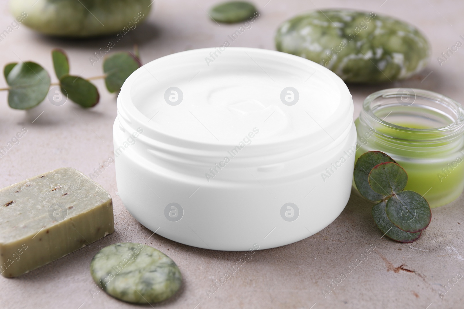 Photo of Jars of cream, soap, spa stones and green leaves on light textured table, closeup. Body care products