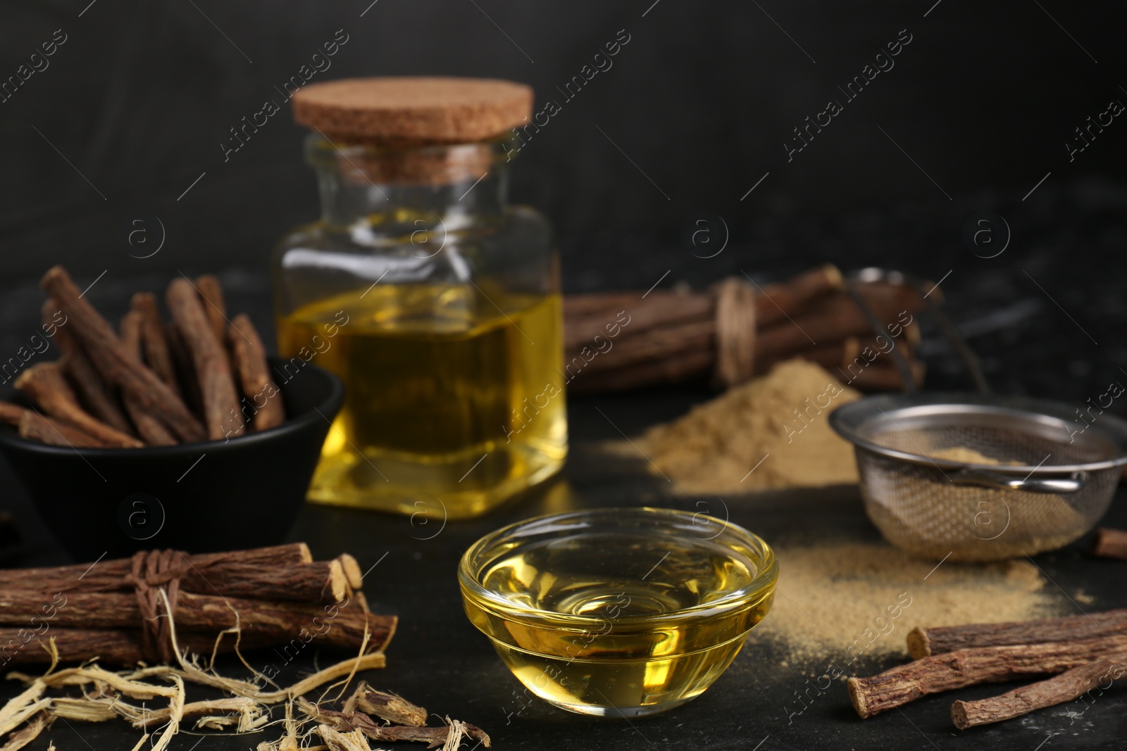 Photo of Dried sticks of licorice roots, powder and essential oil on black table. Space for text