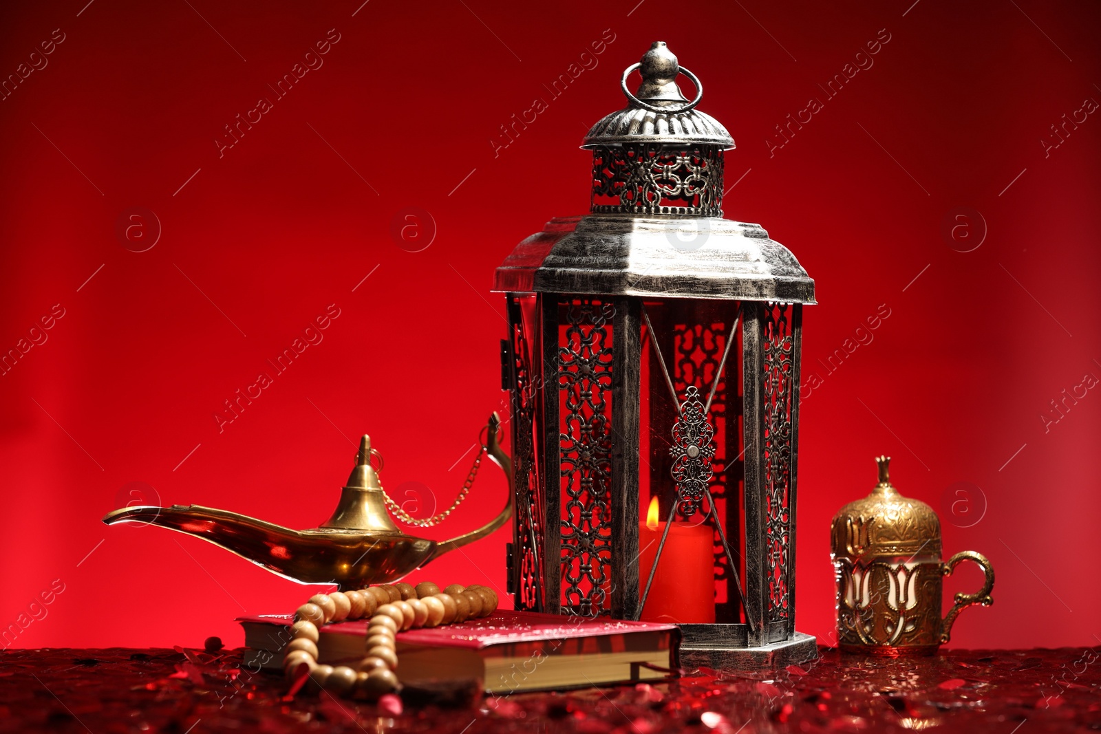 Photo of Arabic lantern, Quran, misbaha and Aladdin magic lamp on shiny red table