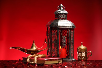 Photo of Arabic lantern, Quran, misbaha and Aladdin magic lamp on shiny red table