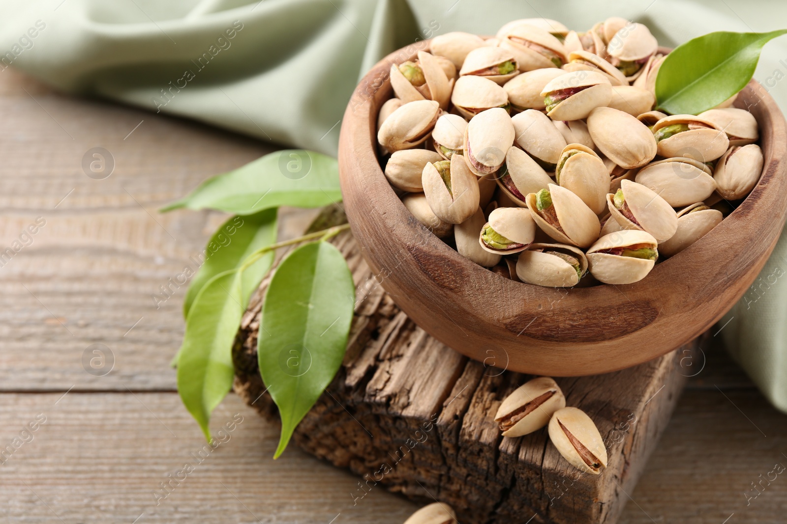 Photo of Delicious pistachios in bowl on wooden table, closeup